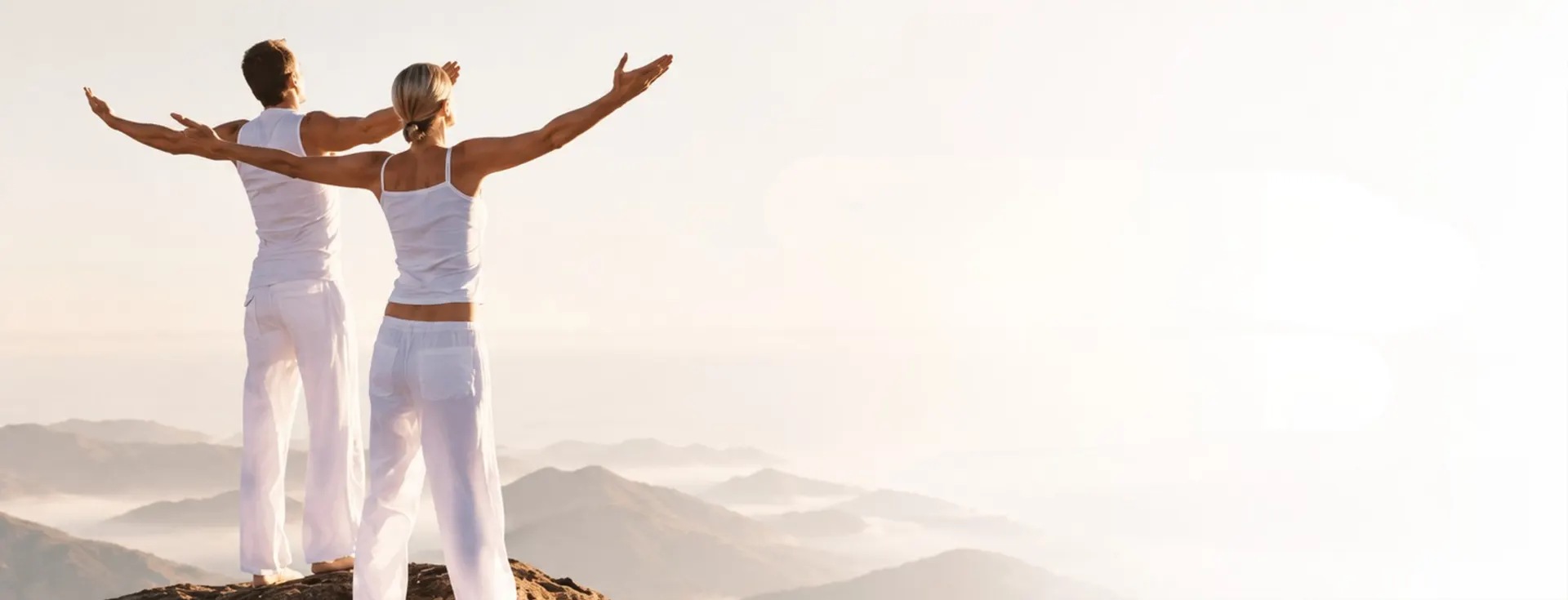 Two people with open arms on a mountain top above the clouds